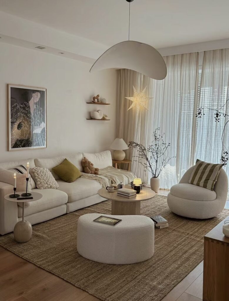 Elegant home decor, The room is bathed in soft, natural light streaming in through large, floor-to-ceiling windows framed with sheer, ivory curtains. The walls are painted a subtle, warm beige, providing a perfect backdrop for the room’s refined decor.